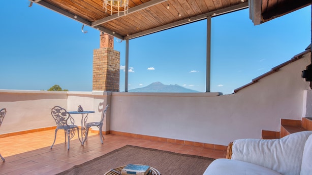 A balcony with a view of a mountain, a brick fireplace, and a seating area with a table and chairs. - Villa Desiderio The Belvedere (Angri)