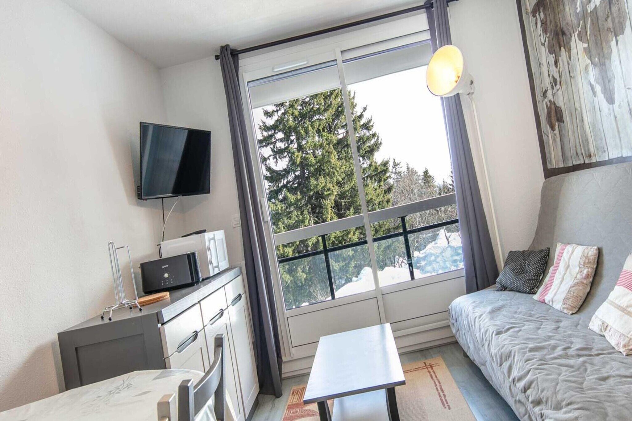 A room with a bed, a desk, a television, and a window with a view of trees.