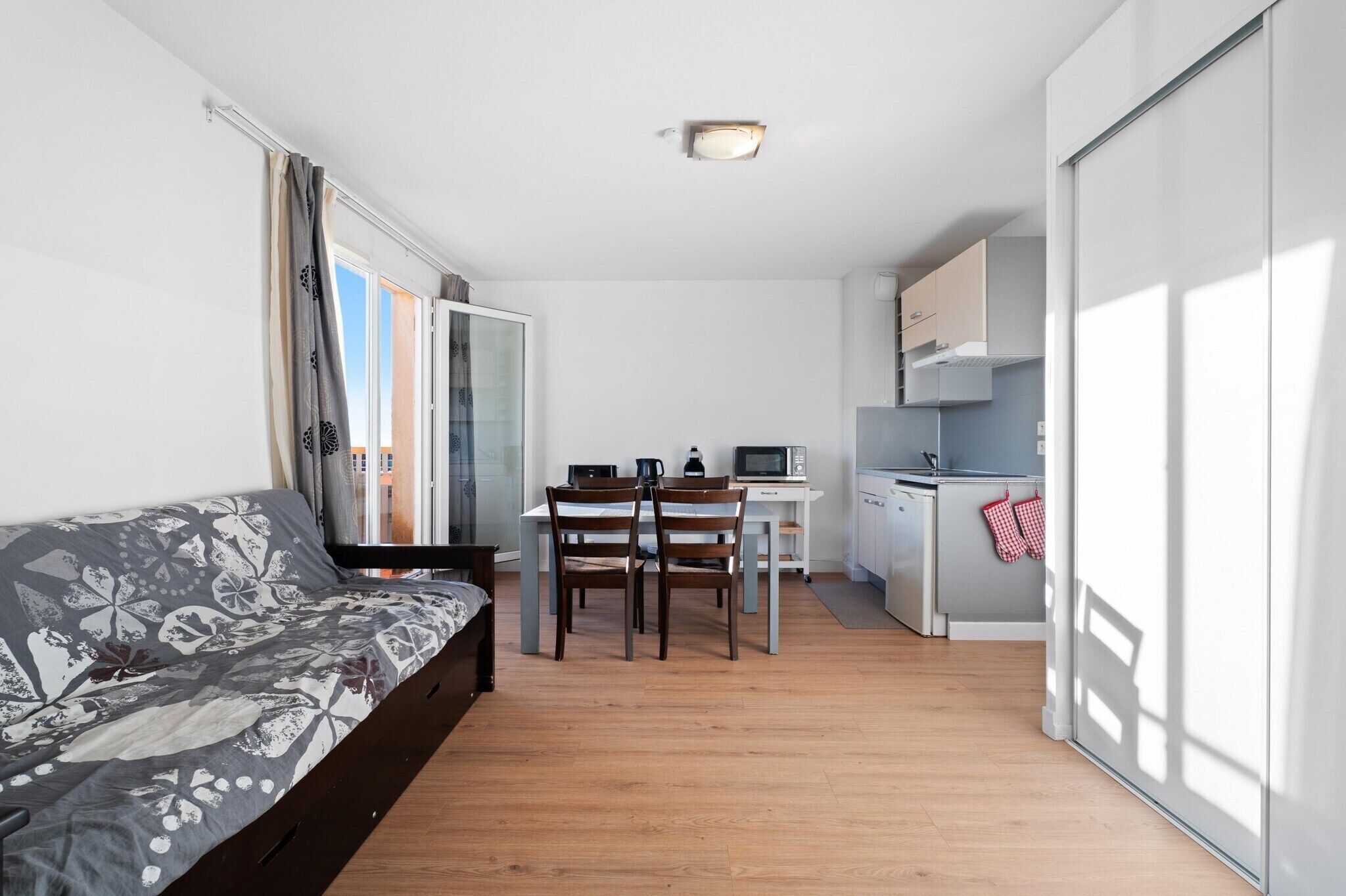 Un espace de vie compact comprenant un canapé, une table à manger, des chaises, un coin cuisine et une porte-fenêtre coulissante.