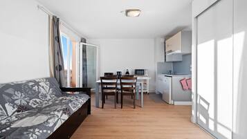 Un espace de vie compact comprenant un canapé, une table à manger, des chaises, un coin cuisine et une porte-fenêtre coulissante.