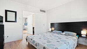 Un dormitorio con cama, lámparas de noche, armario y puerta que da a un baño.