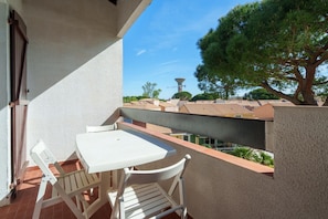 Ein Balkon mit einem weißen Tisch und Stühlen, mit Blick auf eine Wohngegend mit Häusern und einem großen Baum.