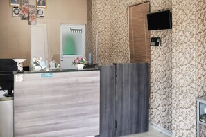 Een receptiegedeelte met een houten receptiebalie, een aan de muur bevestigde televisie, een telefoon en een deur met een geëtste glazen panelen.