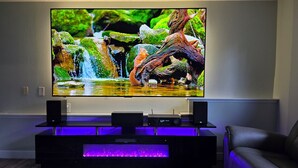 En platt-TV monterad på väggen, med en träinredd mediabänk under som har en inbyggd baslåda och en lila LED-ljuslist.