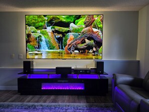 A flat-screen TV mounted on a wall, with a wooden entertainment unit below featuring a built-in subwoofer and a purple LED light strip. - Perfect 5-bedroom house with AC in wonderful Coeur d'Alene (Coeur d'Alene)