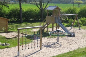 Ein Spielplatz mit Rutsche, Kletternetz und einer Holzkonstruktion.
