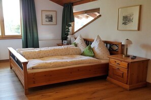 Ein hölzernes Bett mit Kopfteil, ein Nachttisch mit Schubladen, eine Lampe und zwei gerahmte Bilder an der Wand.