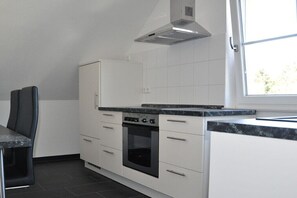 Eine moderne Küche mit weißen Schränken, einem eingebauten Ofen und einem Fenster, das für natürliches Licht sorgt.