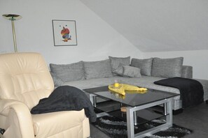 Ein modernes Wohnzimmer mit Sofa, Sesseln und einem Glastisch.