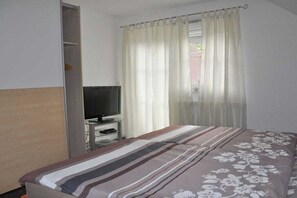 Ein Hotelzimmer mit einem Bett, einem Fernseher auf einem Schrank, einem Fenster mit Vorhängen und einem Kleiderschrank.