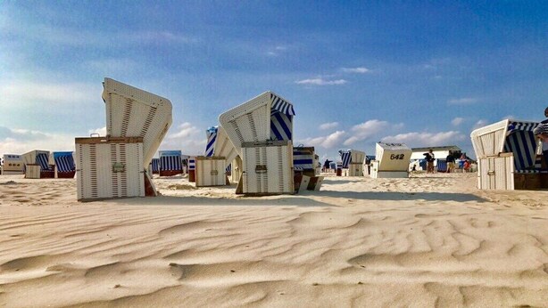 Ein Strand mit Reihen aus weißen Liegestühlen und Sonnenschirmen, einige davon mit Nummern versehen.