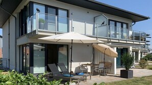 Ein modernes, zweistöckiges Haus mit Balkon, Sitzgelegenheit im Freien und einem großen Fenster.