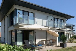 Ein modernes, zweistöckiges Haus mit Balkon, Sitzgelegenheit im Freien und einem großen Fenster.