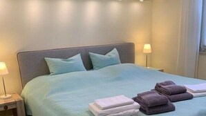 Ein ordentlich bezogenes Bett mit einer hellblauen Tagesdecke, zwei Kissen und gefalteten Handtüchern.