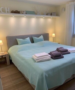 Ein ordentlich bezogenes Bett mit einer hellblauen Tagesdecke, zwei Kissen und gefalteten Handtüchern.