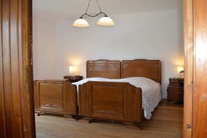 A wooden bed with a white bedspread, two bedside lamps, and a hanging light fixture. - Holiday apartment with 2 bedrooms (Merzig-Bietzen)