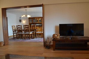 A living room with a wooden dining table, chairs, a TV stand, and a chandelier. - Holiday apartment with 2 bedrooms (Merzig-Bietzen)