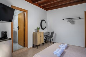A room with a bed, a desk, a chair, a television, a mirror, and a towel rack. - Pinotsi Room 1- Double bed (Simi)