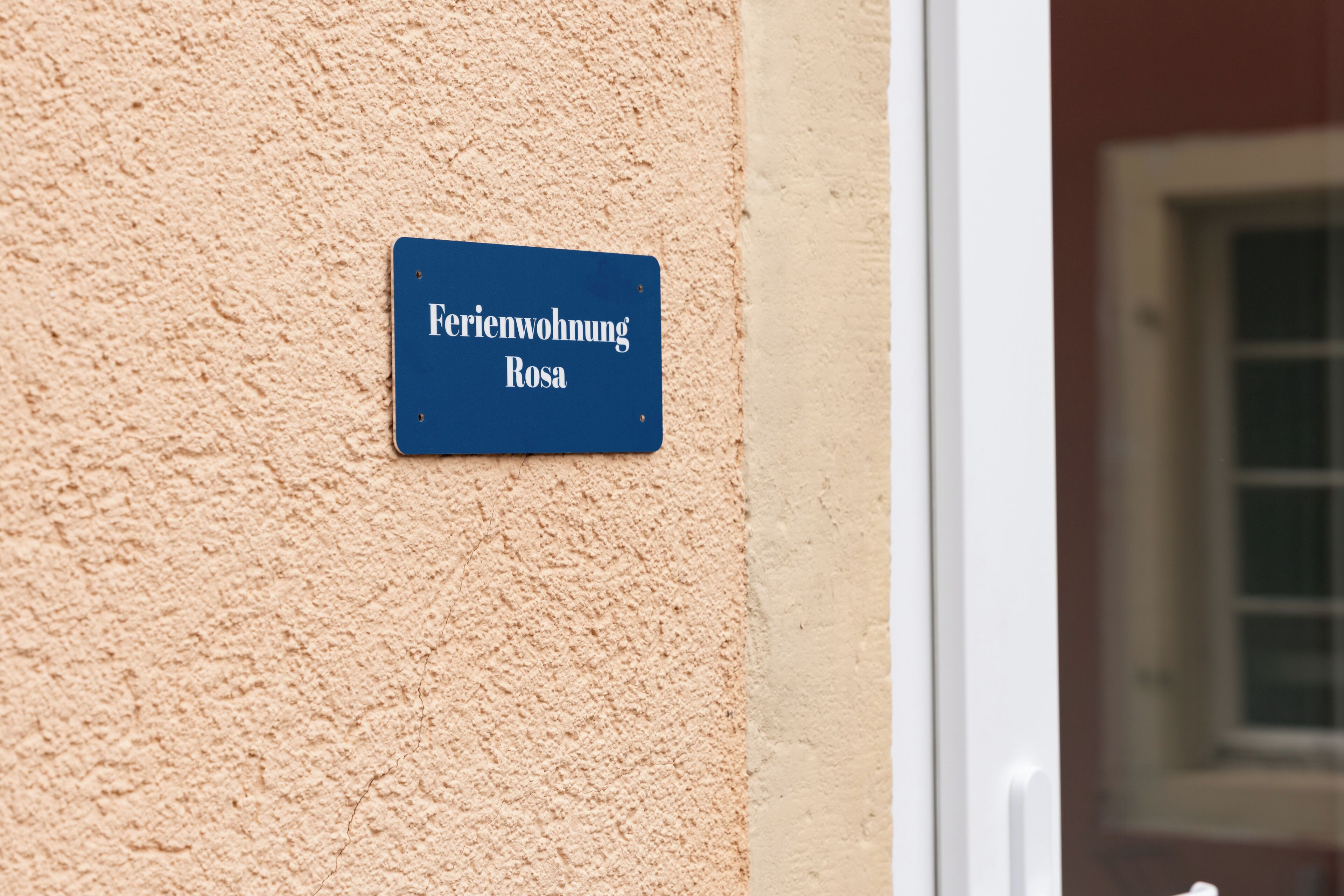 A blue sign with white text on a textured wall, indicating a location named 'Feriendorf Rosa.'