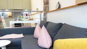 En grå sofa med pink og gule puder, et hvidt sofabord, og et køkken i baggrunden.