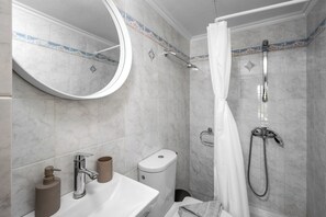 A bathroom with a sink, mirror, toilet, shower, and towel rack. - Pinotsi Room 3- Double bed (Simi)
