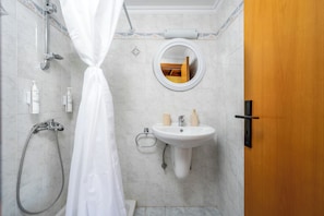 A bathroom with a shower, sink, mirror, and a wooden door. - Pinotsi Room 4- Double bed (Simi)
