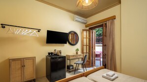 Habitación de hotel con dos camas, un escritorio, televisor, armario y vista a través de una puerta.