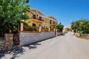 A two-story building with balconies, a stone wall, and a clear sky. - Pinotsi Room 5 -2 single (Simi)