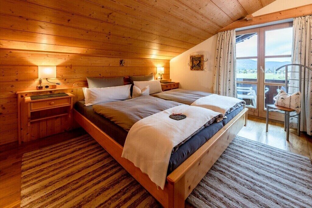 Ein Schlafzimmer einer Holzhütte mit zwei Betten, einem Nachttisch, einer Lampe und Blick ins Freie.