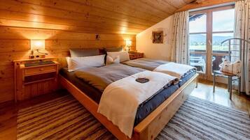 Ein Schlafzimmer einer Holzhütte mit zwei Betten, einem Nachttisch, einer Lampe und Blick ins Freie.