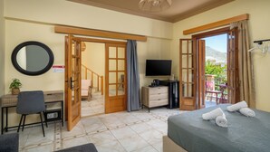 Quarto de hotel com cama, escrivaninha, cadeira, televisão e varanda com cadeiras.