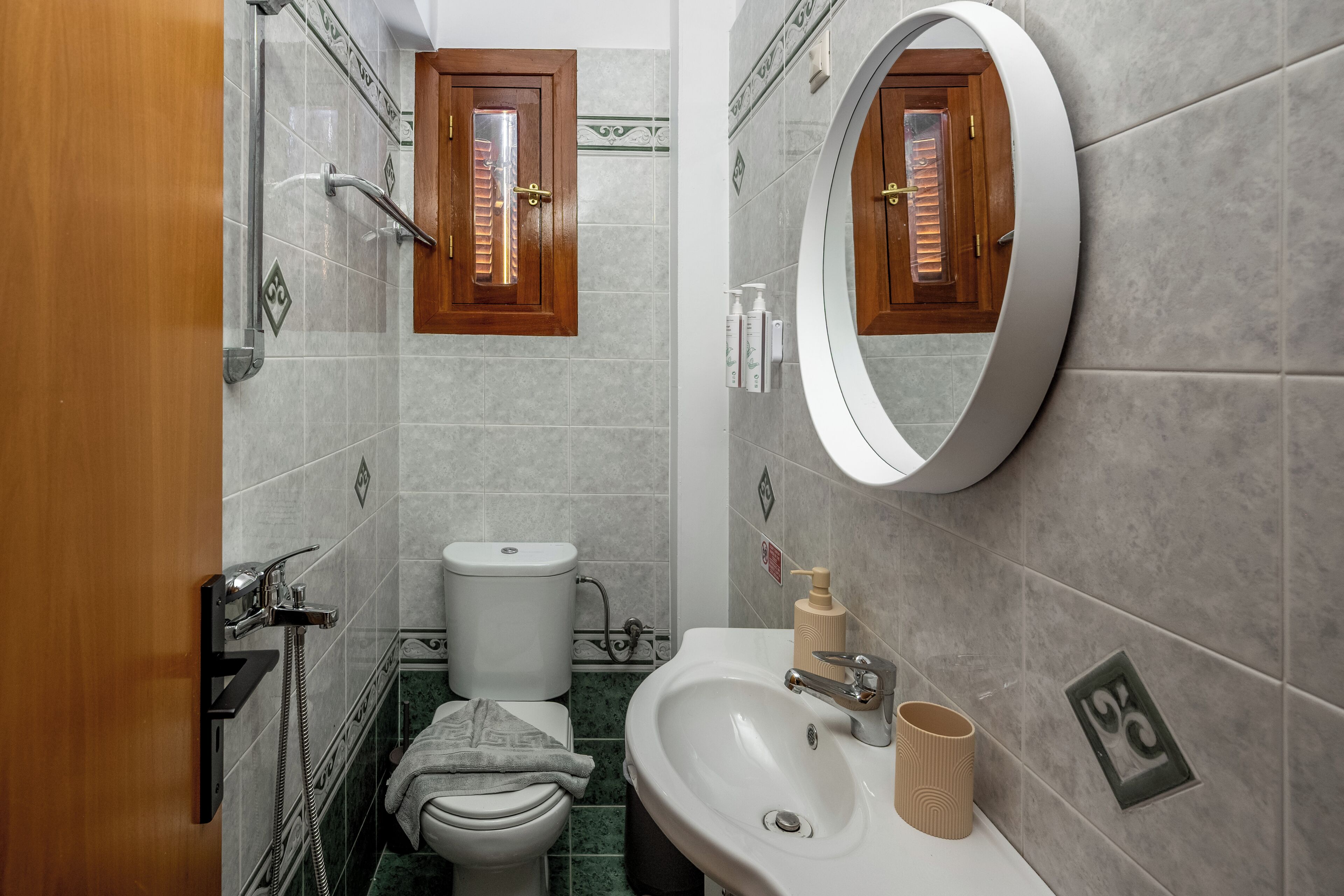 Un baño con inodoro, lavamanos, espejo, ducha y perchero para toallas.