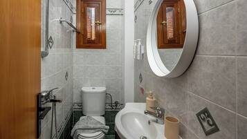 Un baño con inodoro, lavamanos, espejo, ducha y perchero para toallas.