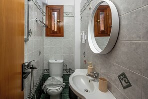 A bathroom with a toilet, sink, mirror, shower, and towel rack. - Pinotsi Room 6- ground floor (Simi)