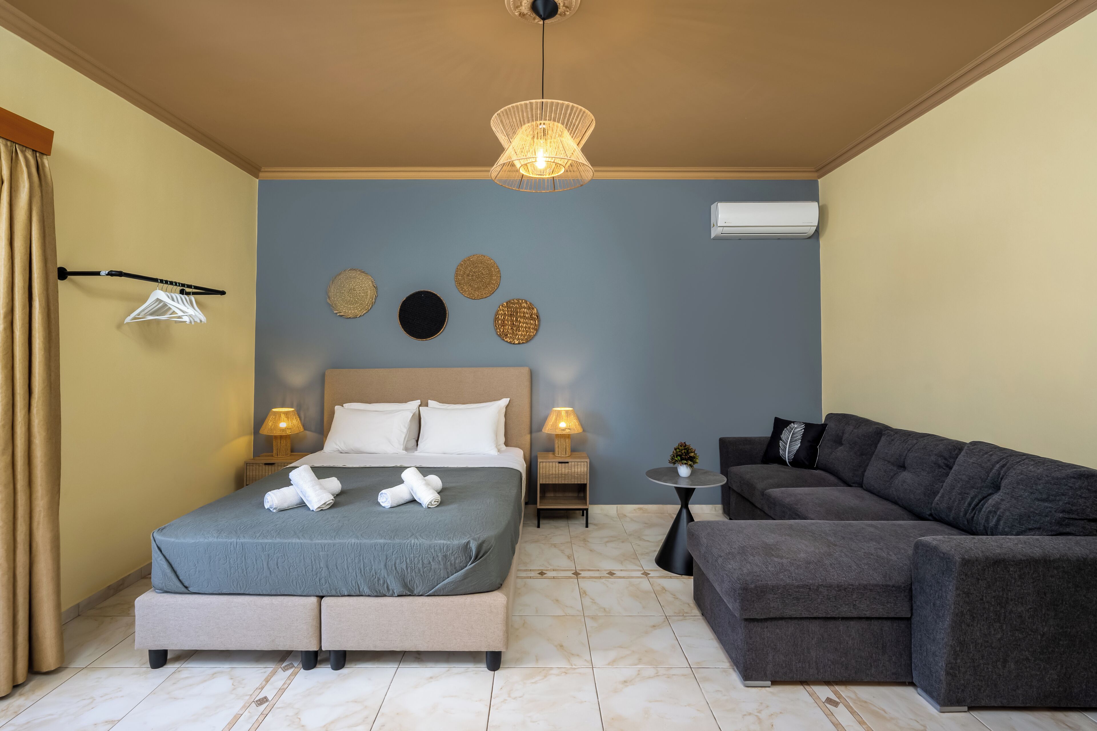 Un dormitorio con cama, lámparas de noche, aire acondicionado instalado en la pared y un sofá gris.