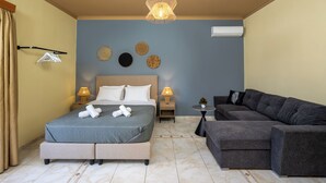 Quarto com cama, abajures, ar-condicionado na parede e sofá cinza.