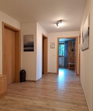 Ein Flur mit Holzboden, einer Tür links, einem Bild an der Wand und einem Fenster rechts.