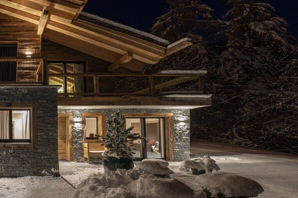 A two-story log cabin with a stone foundation, a balcony, and a snow-covered landscape. - Holiday apartment Sëléna (Bruson)