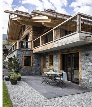 A two-story building with a stone facade, wooden balconies, and a patio area with outdoor seating. - Holiday apartment Sëléna (Bruson)