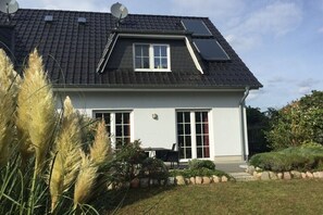 A house with a sloped roof, satellite dish, and a small garden with plants and a table. - Holiday home in Zierow with swimming pool (Zierow)