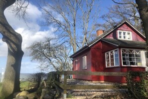 A red house with a wooden fence, surrounded by trees and a clear sky. - Holiday home in Zierow with swimming pool (Zierow)