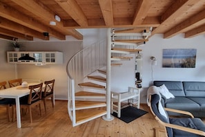 Eine Wendeltreppe in einem modernen Innenraum mit Holzbalken, einem Essbereich und einem grauen Sofa.