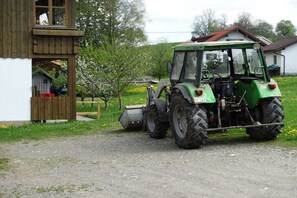 A green tractor parked on a gravel path next to a wooden structure with a window. - Holiday apartment with 2 bedrooms (Nesselwang)