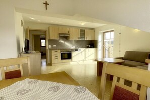 A kitchen with wooden cabinets, a stove, and a dining area with a table and chairs. - Holiday apartment with 2 bedrooms (Nesselwang)