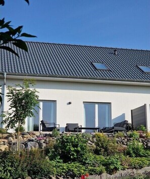 Ein modernes Haus mit geneigtem Dach, einer Steinsichtmauer und einer Terrasse mit Sitzgelegenheiten.