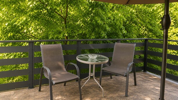 Ein Balkon mit zwei Stühlen und einem Tisch, umgeben von einem schwarzen Geländer und Grünpflanzen.