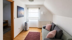 Ein modernes Wohnzimmer mit einem grauen Sofa, einem roten Teppich, einem Standheizkörper und einem Fenster mit Vorhängen.