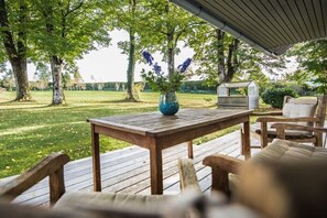 Eine Holzterrasse mit Tisch und Stühlen, eine Vase mit Blumen und eine kleine Struktur im Hintergrund.