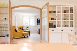 Ein Zimmer mit einem gelben Sessel, einem Esstisch, einer weißen Vitrine und einem hölzernen Bogen.