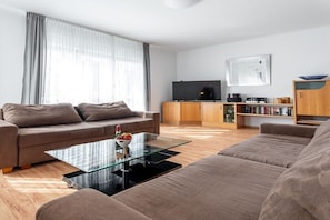 Ein modernes Wohnzimmer mit einer Couch, einem Glastisch, einem Fernseher und einem Bücherregal.